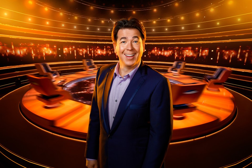 a man in a suit stands in front of a stage with chairs