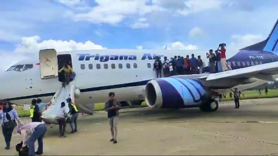 people boarding a trigana airplane on a sunny day