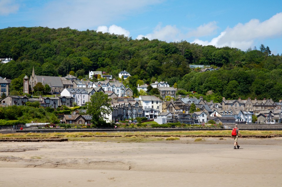 a man with a red backpack walks across a sandy beach in front of a small town