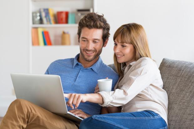 a man and woman sit on a couch looking at a laptop