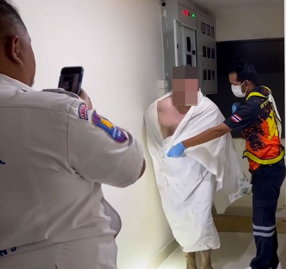 a man wrapped in a towel is being photographed by a man wearing a shirt that says emergency