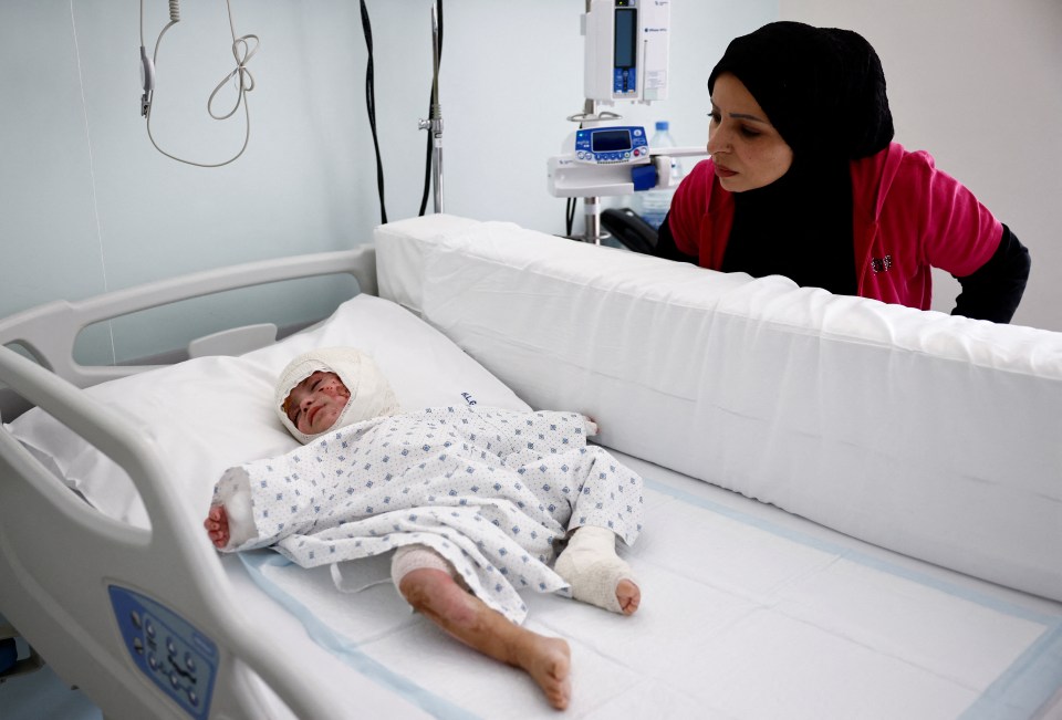 a woman in a pink shirt stands next to a baby in a hospital bed