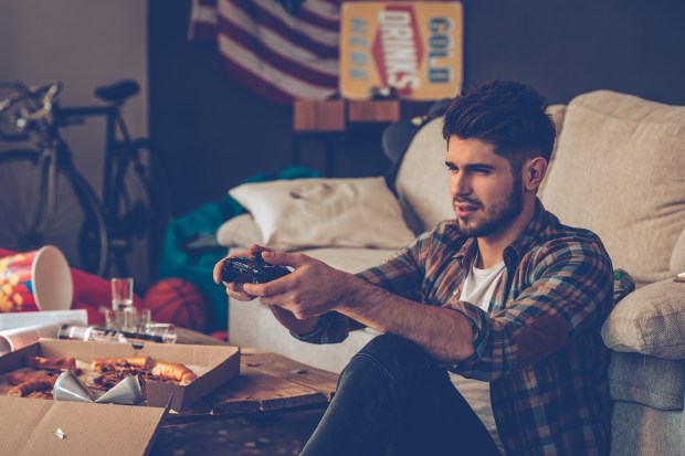 a man sits on a couch playing a video game in front of a sign that says cold drinks