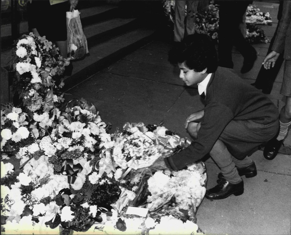 a person kneeling down in front of a pile of flowers