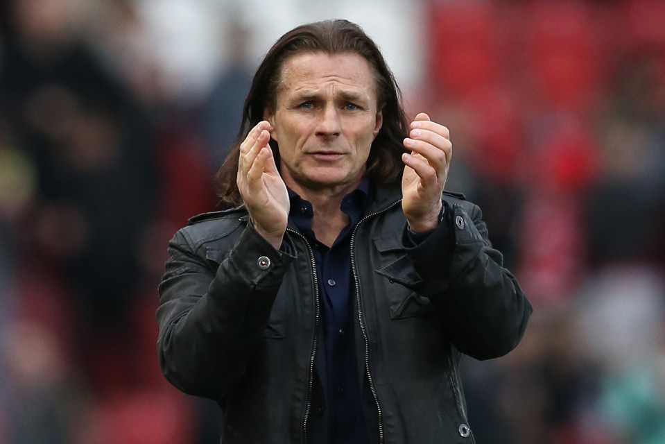 a man with long hair wearing a black jacket applauds