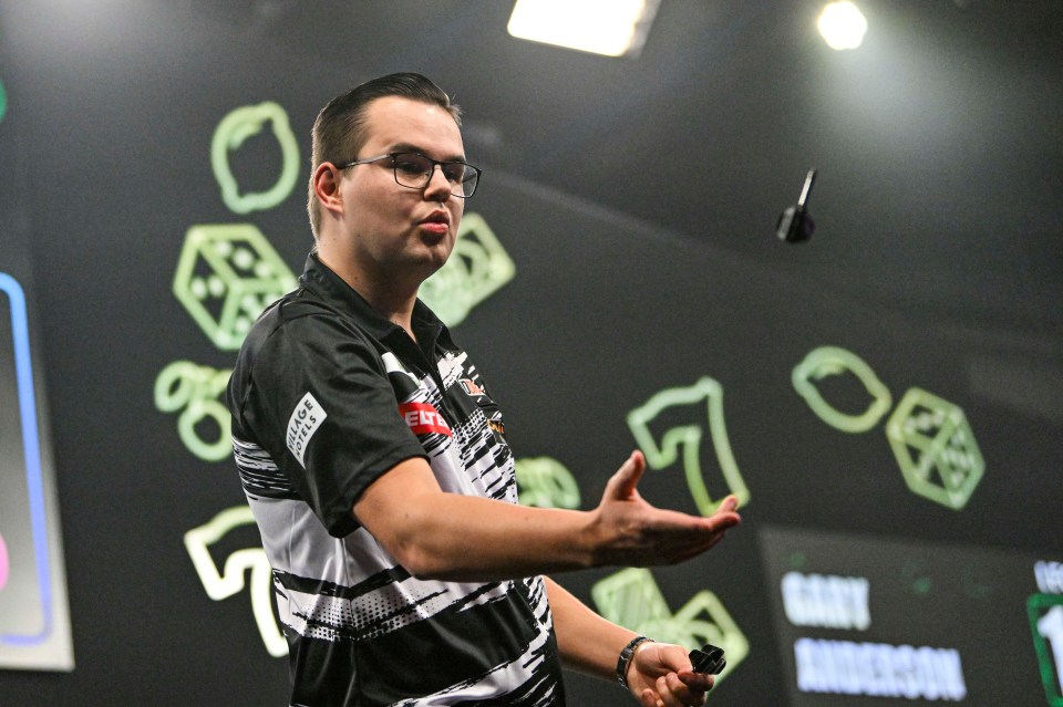 a man throws a dart in front of a sign that says gary anderson