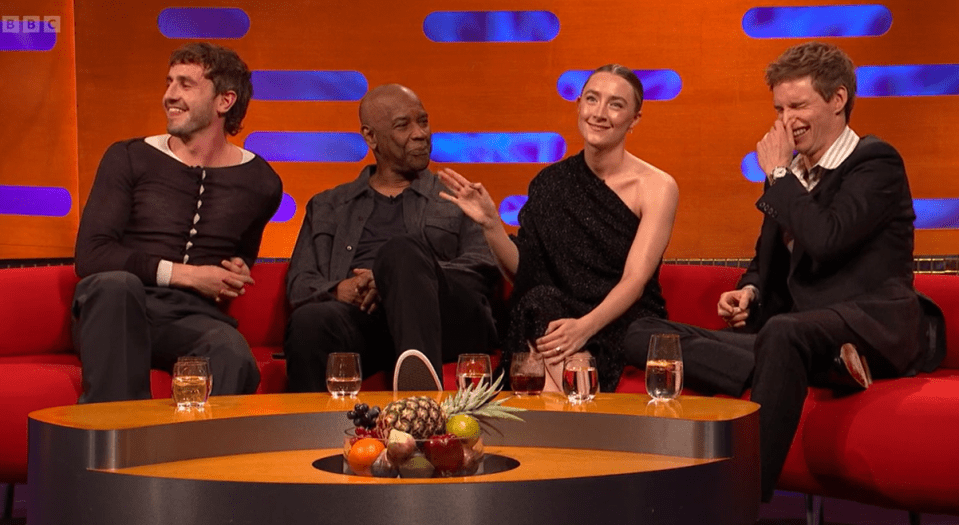 four people sit around a table with a bbc logo on the wall behind them