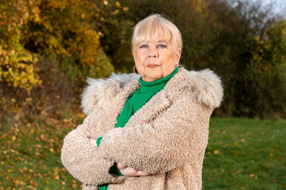 a woman in a fur coat and green sweater stands with her arms crossed