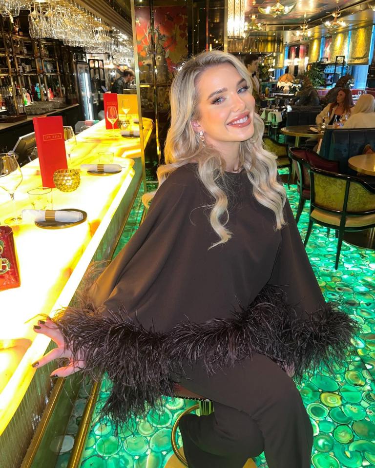 a woman in a black top with feathers on the sleeves sits at a bar