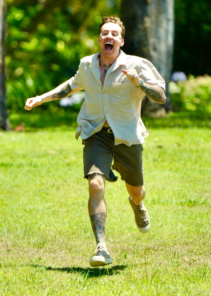 a man with tattoos is running in the grass with his mouth open