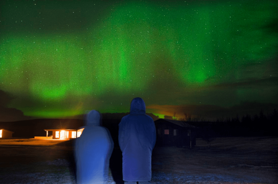 two people standing in front of a house looking at the aurora borealis