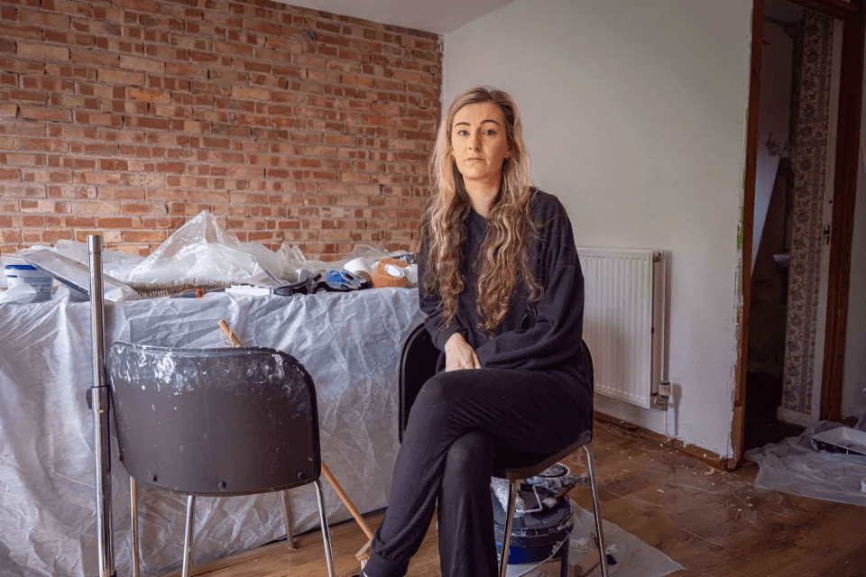 a woman sits in a chair in front of a brick wall