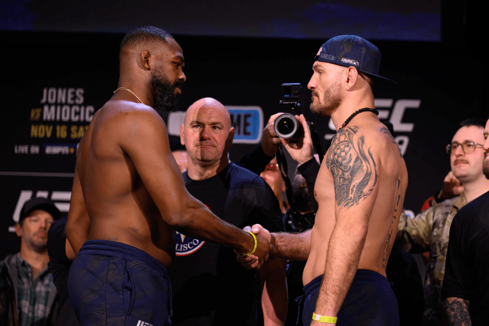 two men shake hands in front of a sign that says jones miocic