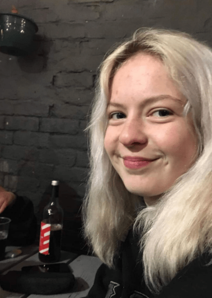 a woman with blonde hair is smiling in front of a bottle of coca cola