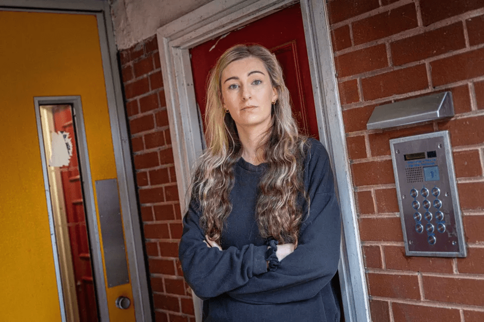 a woman stands in front of a red door with her arms crossed