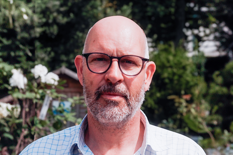 a bald man with glasses and a beard looks at the camera