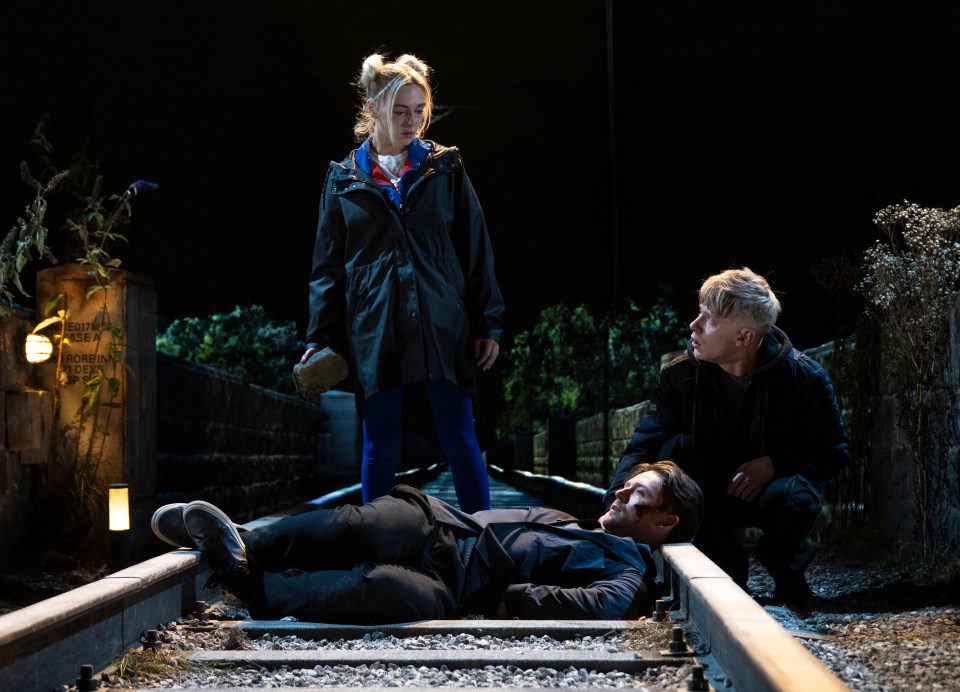 a man is laying on the train tracks while a woman and a man look on