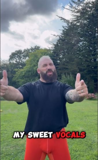 a man with a beard is giving a thumbs up in a field .