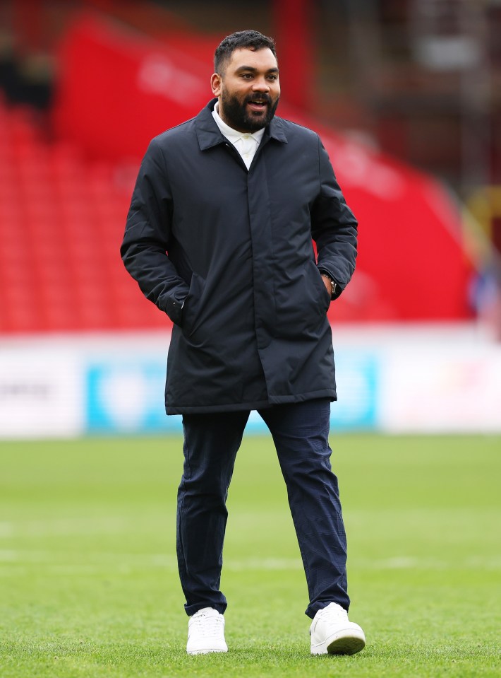 a man in a black coat stands on a soccer field