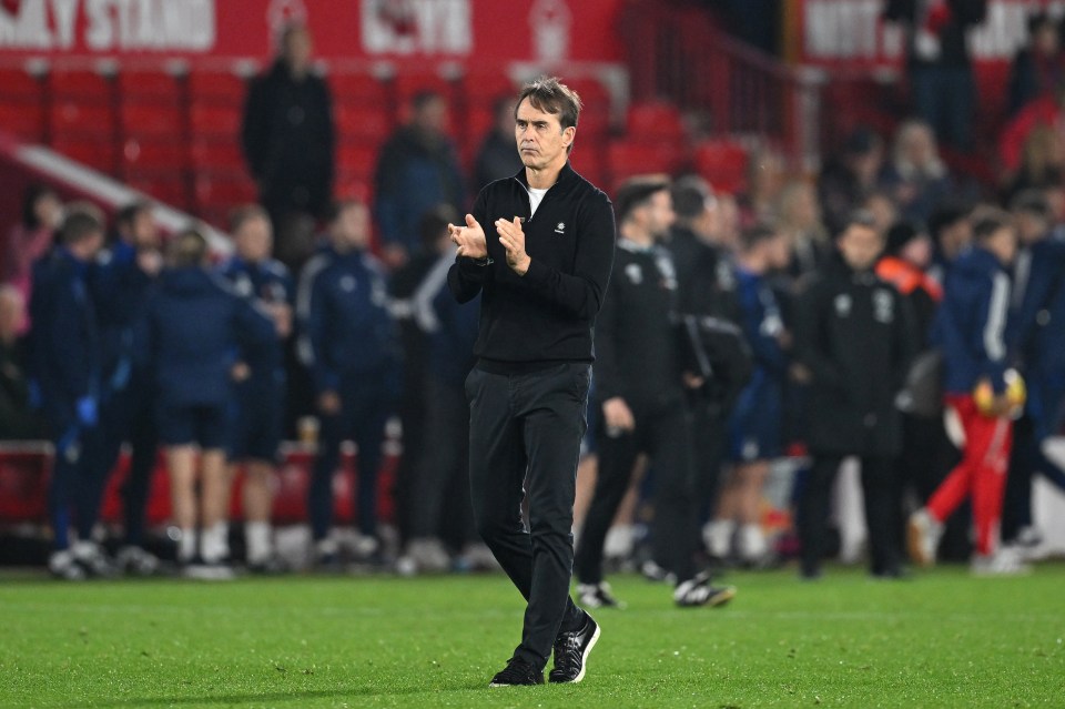 a man in a black jacket applauds on a soccer field