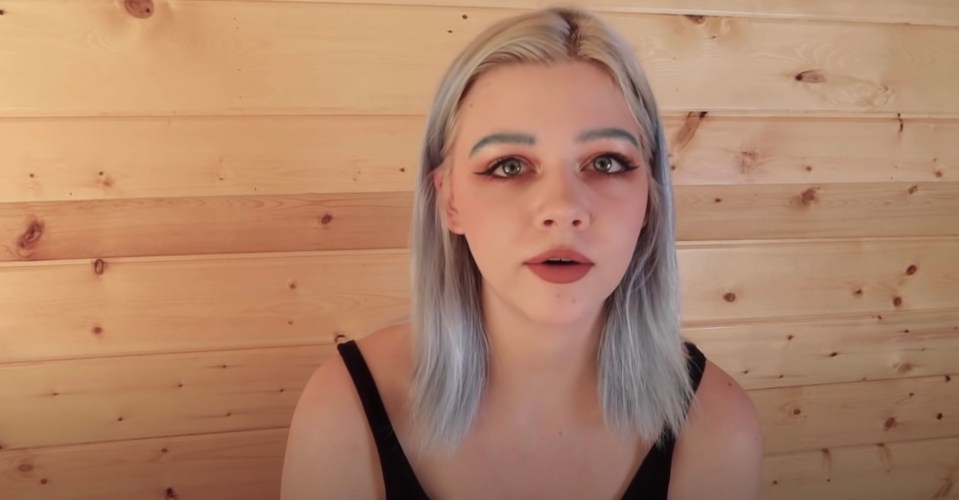 a woman with blue eyebrows is standing in front of a wooden wall