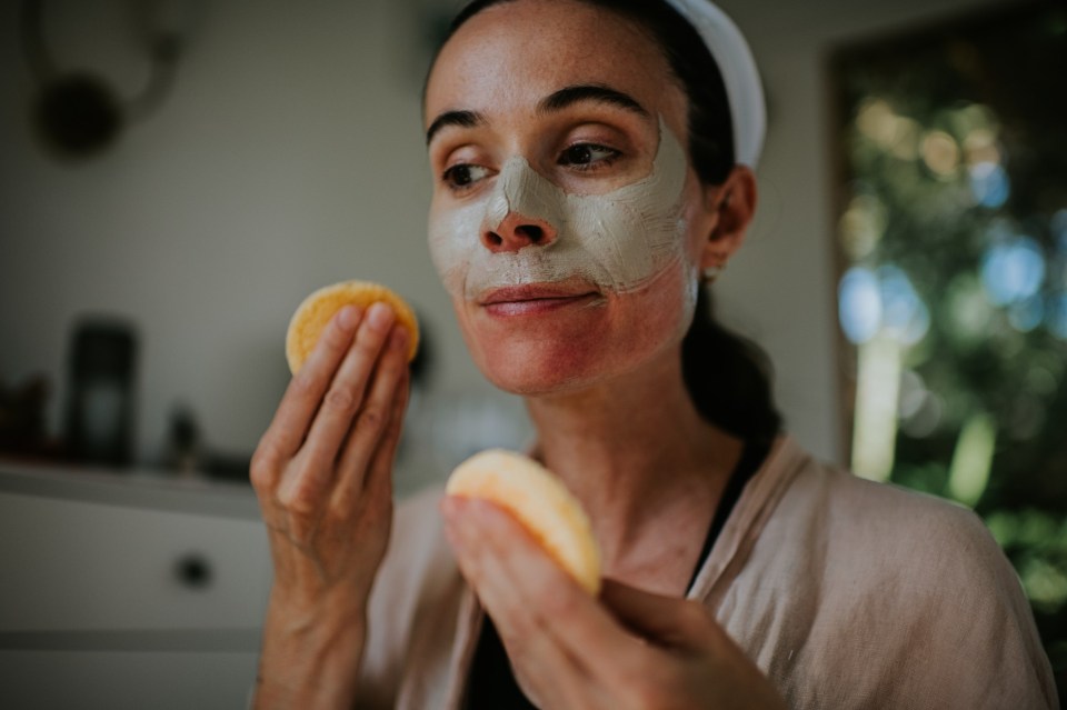 a woman is applying a clay mask to her face