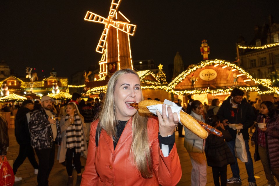 a woman eating a sausage in front of a windmill that says ' caffe ' on it