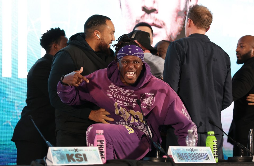 a man in a purple hoodie is sitting in front of a sign that says ksi