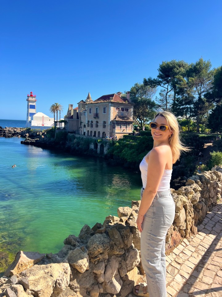 a woman stands in front of a lighthouse overlooking a body of water