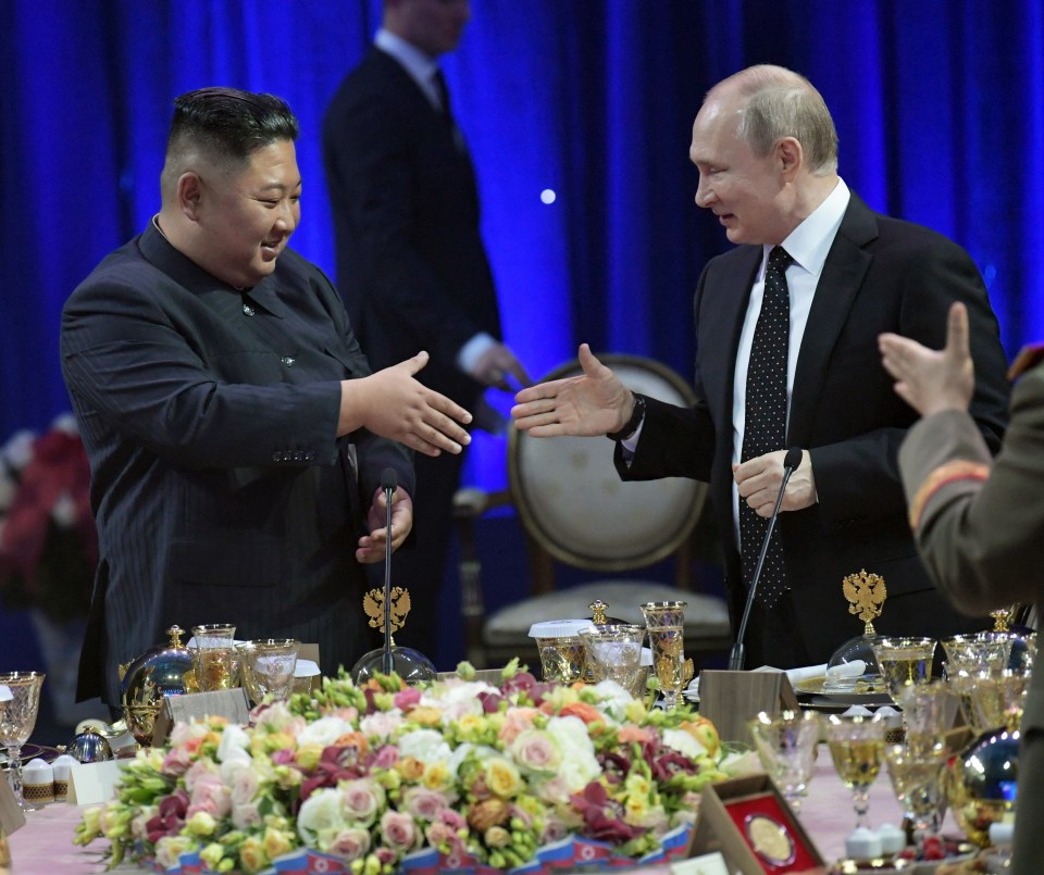 a man in a suit talks to another man in front of a table full of flowers