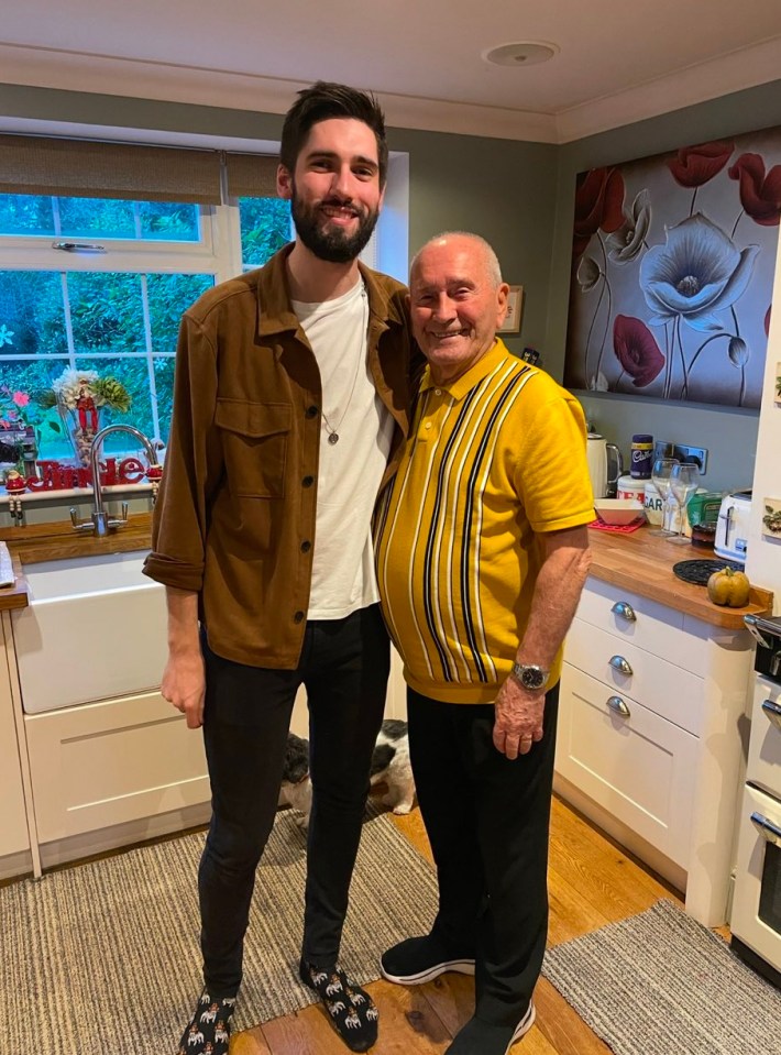 a man in a brown jacket stands next to an older man in a yellow shirt