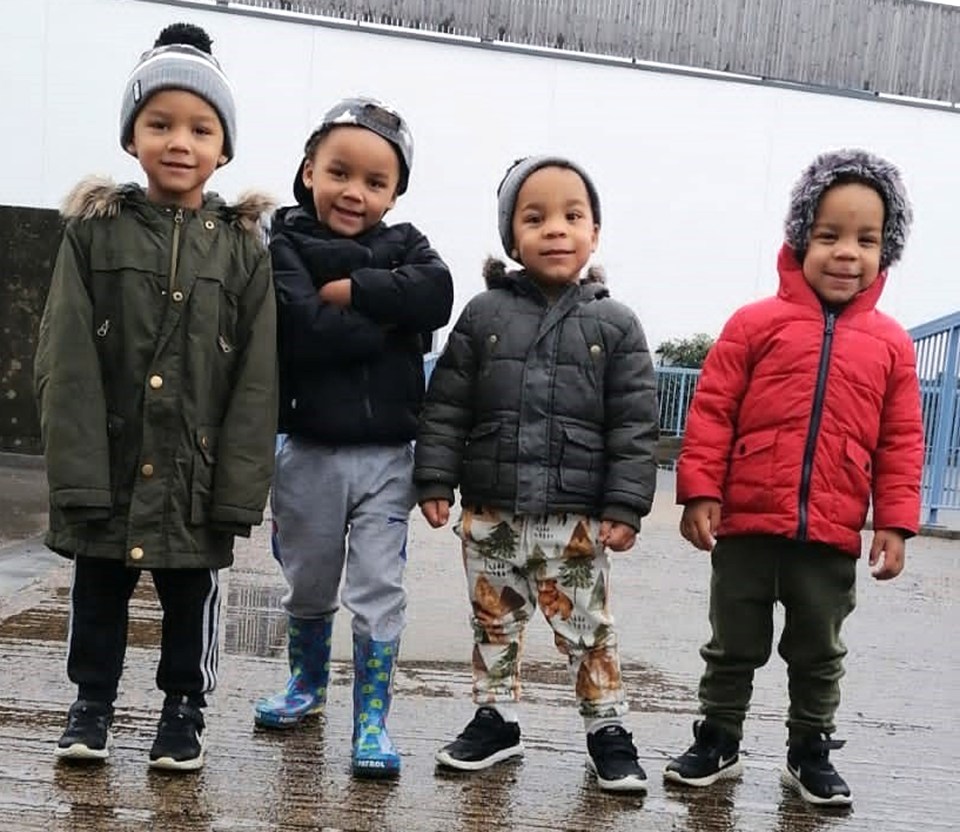 four young boys standing next to each other with one wearing a red jacket