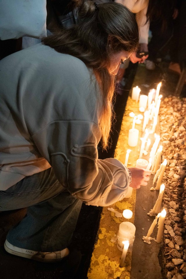 a woman kneeling down lighting a candle in front of a row of lit candles