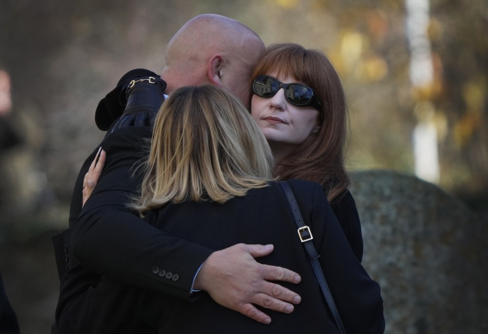 a man in a suit is hugging two women one of whom is wearing sunglasses