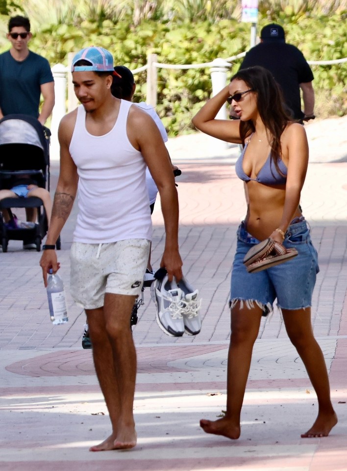 a woman in a bikini and a man in a tank top walk barefoot