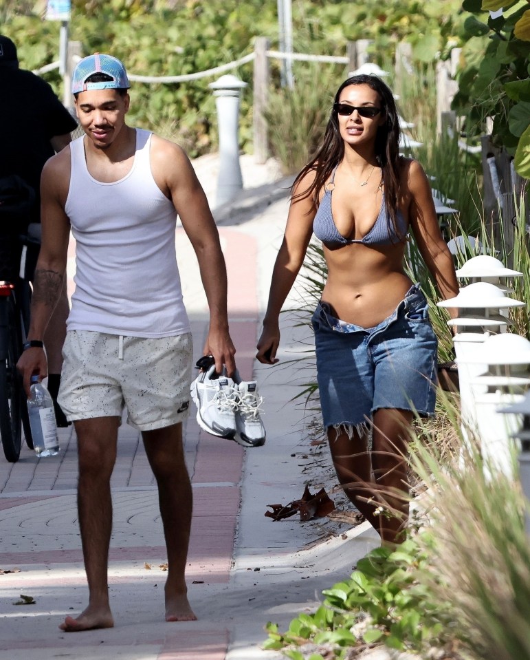 a man in a white tank top walks next to a woman in a bikini