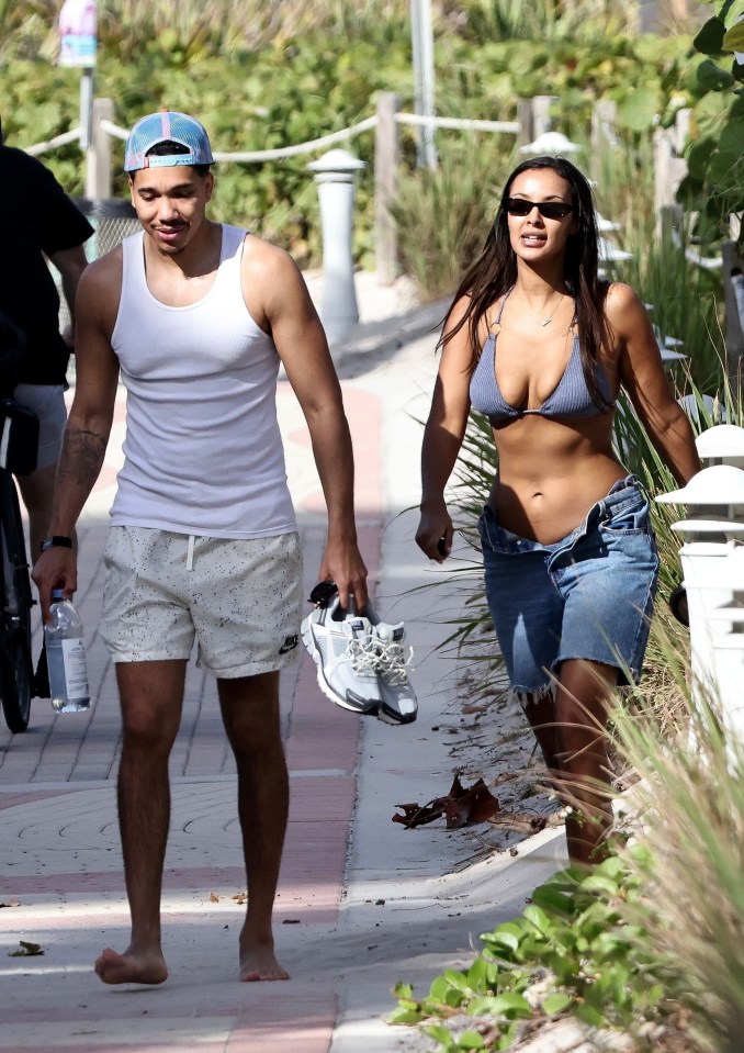 a woman in a bikini and a man in a tank top walk down a sidewalk