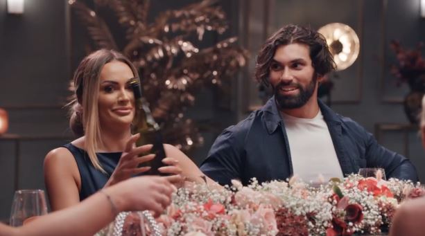 a man and a woman are sitting at a table with flowers and a bottle of wine .