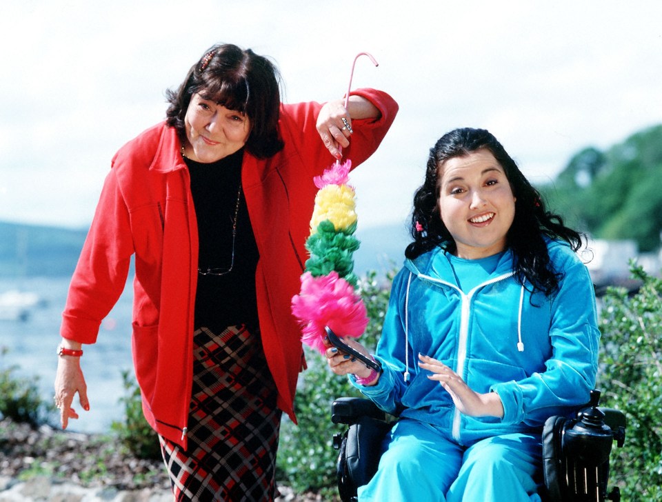 a woman in a red jacket is standing next to a woman in a wheelchair