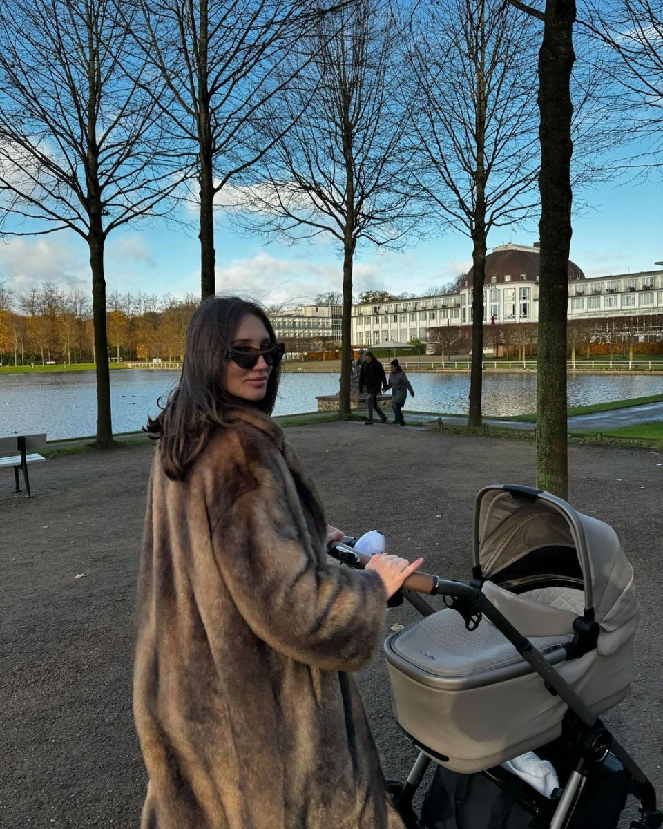 a woman in a fur coat pushes a stroller in a park