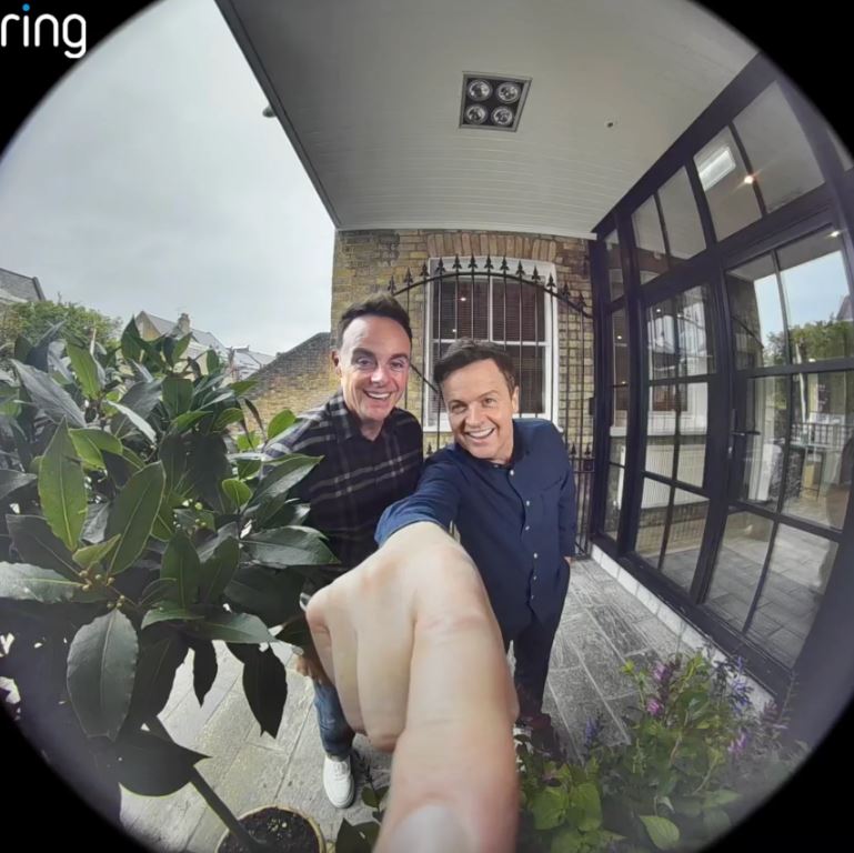 two men are posing for a picture in front of a ring doorbell