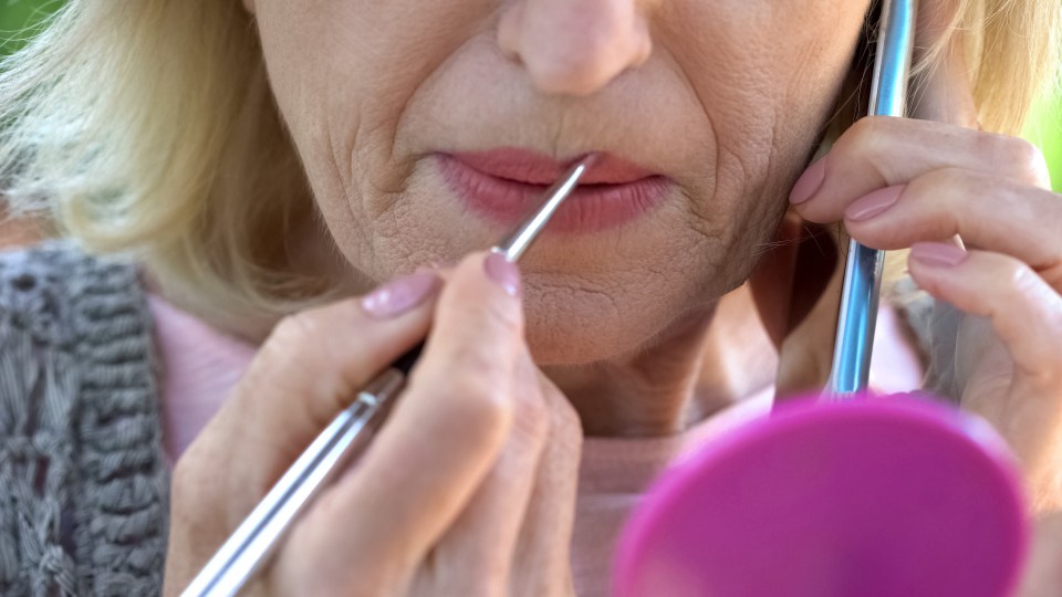 a woman is applying lip gloss in front of a mirror