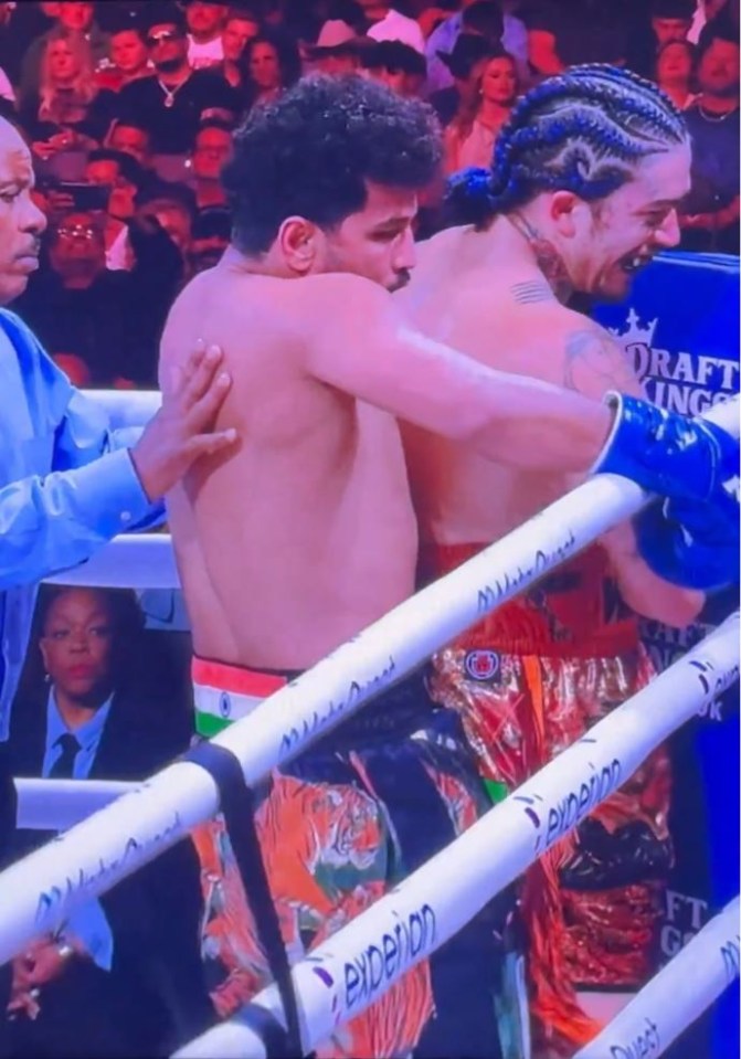 two boxers are hugging in a ring with evidence on the ropes