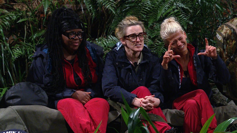 three women are sitting on a rock in the jungle and one of them is wearing glasses