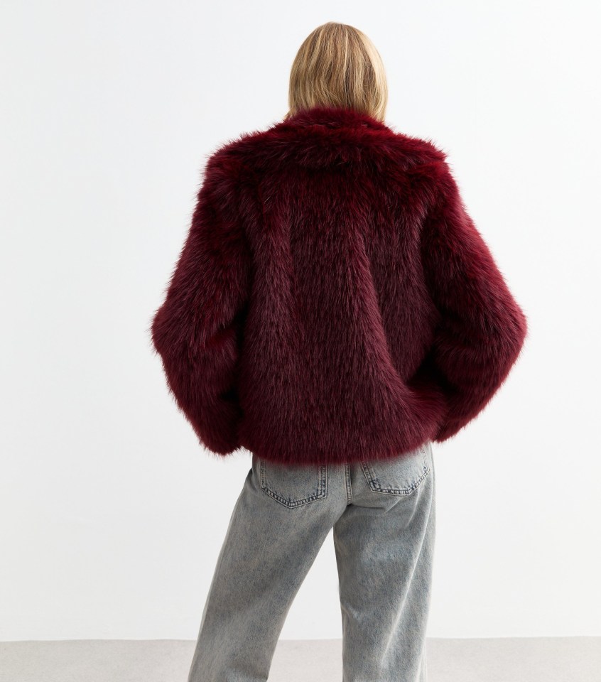 a woman wearing a burgundy faux fur jacket and jeans