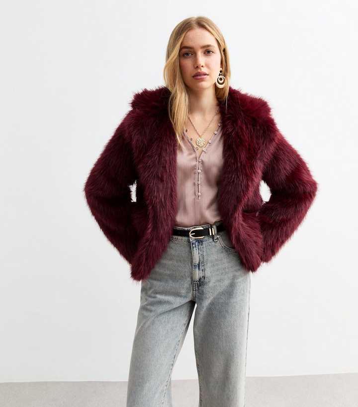 a woman wearing a burgundy faux fur jacket and jeans