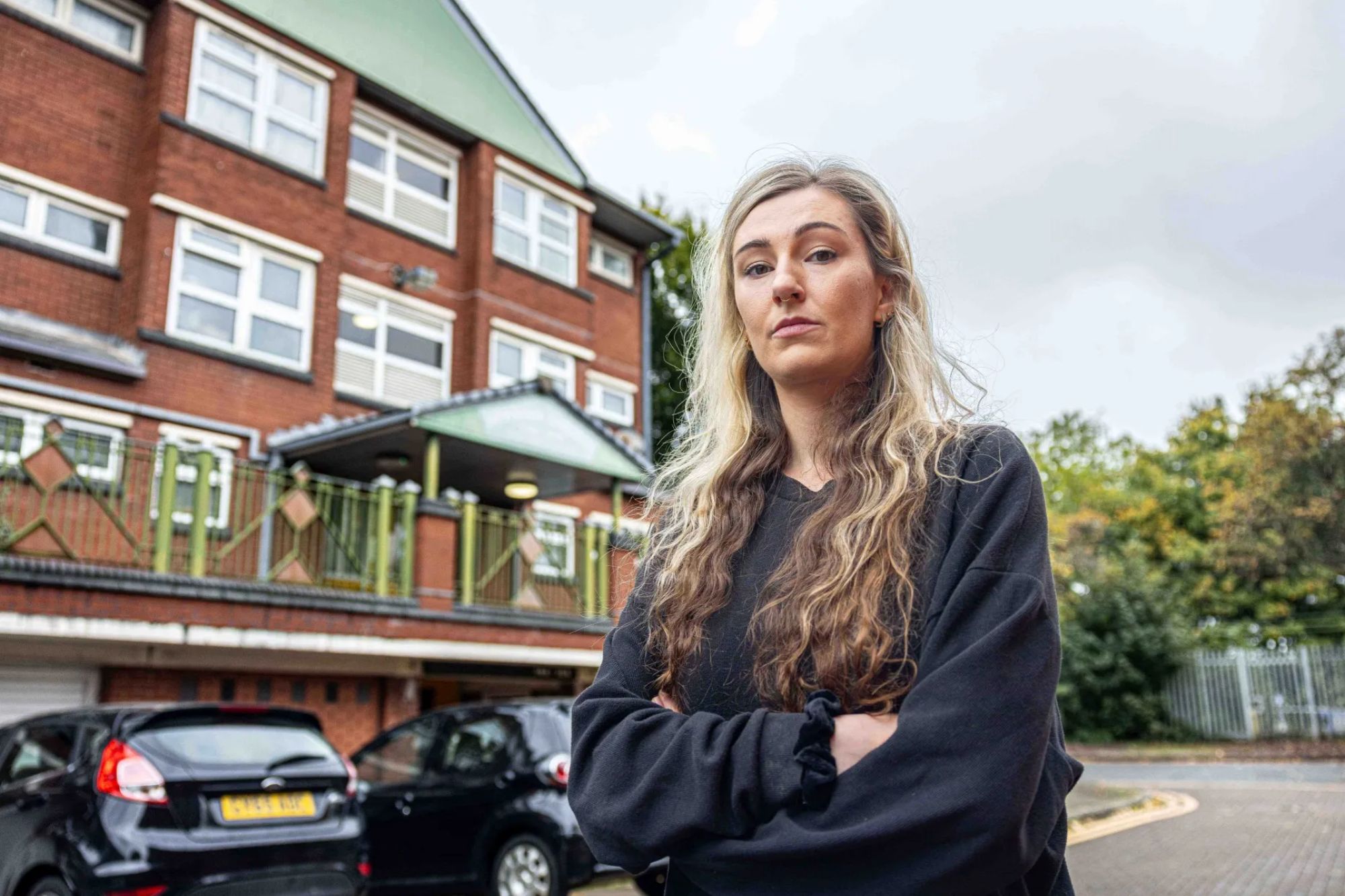 a woman stands in front of a building with her arms crossed