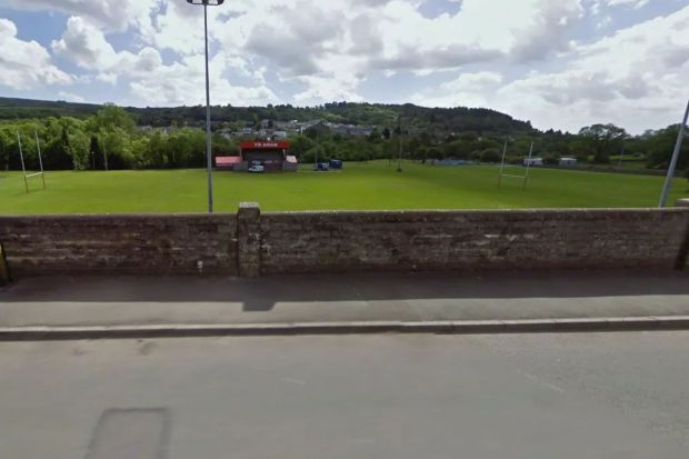 a brick wall surrounds a soccer field with a red building that says st. john 's