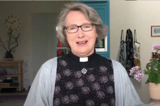 a woman wearing glasses and a clergy collar stands in front of a clock