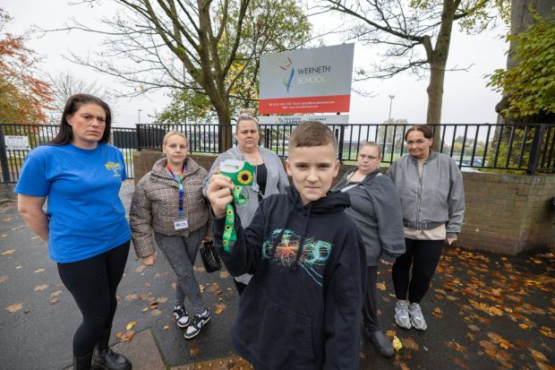 a group of people standing in front of a werneth school sign